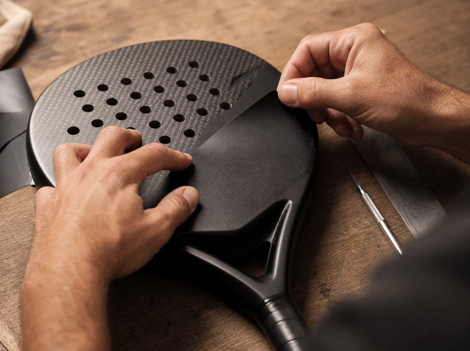 Werkplaatshanden brengen een matte zwarte sticker aan op een custom padel racket
