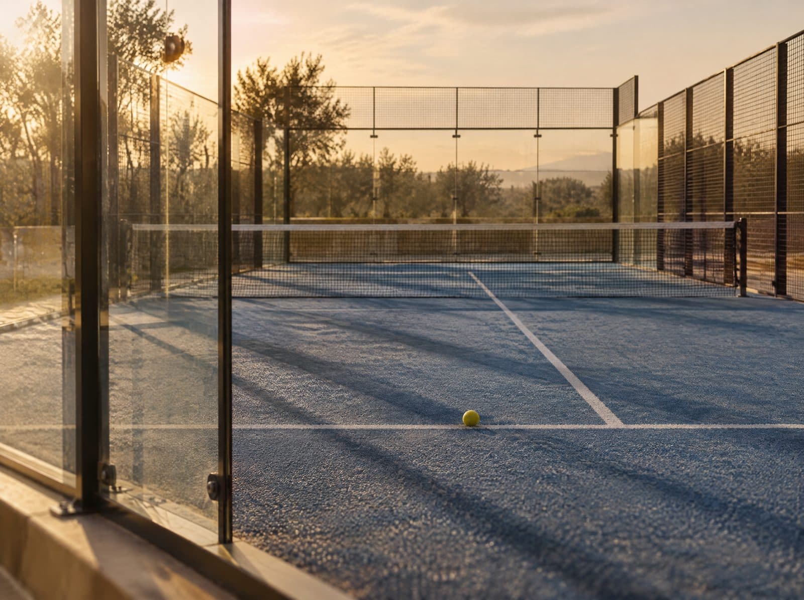 Lege padelbaan met glazen wanden en net in warm avondlicht